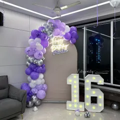 A 'Sweet 16' birthday celebration with a purple and silver color scheme. This home setup features a balloon arch, a personalized neon sign, and large light-up marquee numbers for the perfect photo opportunity.