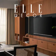 Another shot from the Elle Decor feature, this image highlights the custom floating shelving unit and TV console. The design uses natural teak wood and brass verticals to add texture and warmth, creating a functional yet beautiful focal point in the living area.