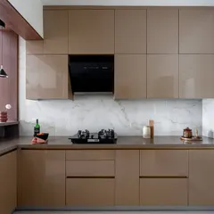 The kitchen features mustard golden laminates with a high-gloss acrylic finish and a white marble-patterned backsplash. The sleek, handleless cabinets contribute to the modern and clean aesthetic.
