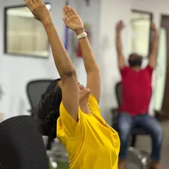 This employee is performing a simple arm stretch while seated, a perfect example of accessible office yoga. This asana helps counteract the hunching posture associated with desk work and opens the chest for deeper breathing.