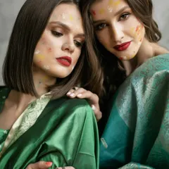 The colors of Holi representing a bond of love and friendship. Two models in matching sarees share a moment of quiet connection, their faces touched with festive colors.