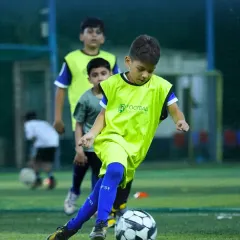 A young player wearing a practice bib focuses intently on dribbling the ball during a training drill. This image captures the concentration and fundamental ball-handling skills we instill in our athletes from a young age.