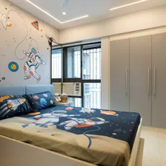 A full view of the space-themed bedroom, showing the neutral gray wardrobe and simple bed frame that balance the playful wallpaper and linens.