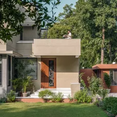 **The Glow House, Ahmedabad:** The exterior of this home is designed to capture the magic of light throughout the day. Tucked into a lush garden, the structure's clean lines and deep porch create a perfect spot for quiet moments, where the architecture itself becomes a frame for the surrounding nature.