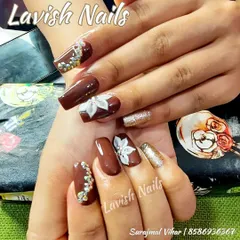 A glamorous set combining brown polish with 3D white floral art, gold glitter accent nails, and cascading crystal patterns for a truly opulent look.
