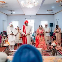 A Sikh couple stands before the Guru Granth Sahib during their Anand Karaj ceremony, a solemn and beautiful moment of their union.