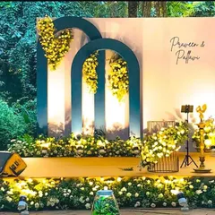 A classy and modern engagement setup for an outdoor event. The deep teal arches with cascading yellow flowers create a stunning contrast against the natural greenery.