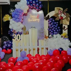 A vibrant 30th anniversary party setup with a purple, white, and red color palette. We used a balloon arch, a 'Happy Anniversary' neon sign, marquee numbers, and decorative pedestals to create a festive atmosphere.