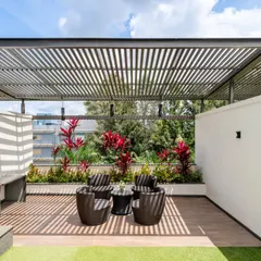 This terrace is all about balanced design. The metal slat pergola creates a beautiful play of light and shadow, providing just enough shade without closing off the sky. A backdrop of vibrant shrubs and a multi-purpose ledge for a pantry or bar make this a highly functional and inviting outdoor living space.