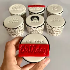 A handheld view of the "It's your birthday" cupcake from the custom set inspired by 'The Office'. The red and white fondant work is crisp and clean, perfect for a fan.
