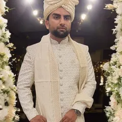 A happy client looking dapper on his wedding day. He wears a custom-fitted, intricately patterned off-white sherwani paired with a matching turban and stole, embodying pure elegance.