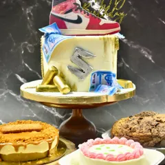 A dessert spread fit for a sneakerhead. The centerpiece is a custom ganache drip cake with a Jordan shoe topper, surrounded by a Biscoff cheesecake, giant cookies, and a mini bento cake.