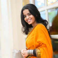 A bright and cheerful portrait of a young woman in a vibrant orange saree, captured in a natural, outdoor urban setting, perfect for a fashion or lifestyle portfolio.