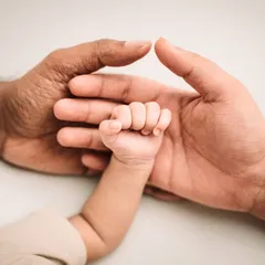 A newborn's tiny fist held between the hands of their parents, a symbol of family strength and unity.