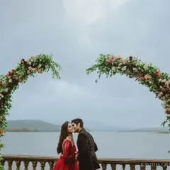 A romantic kiss under a heart-shaped floral arch, set against a serene lake. This is a perfect example of a planned, yet emotionally resonant pre-wedding photograph.