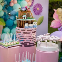 The dessert table is a centerpiece of the celebration. This three-tiered woodland cake, surrounded by themed cake pops and treats, is perfectly integrated into the fairyland decor with its own set of magical mushrooms.