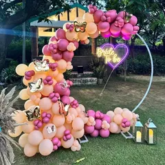 Perfect for a garden or lawn party, this crescent-shaped balloon arch uses a mix of pastel and bright pink balloons. The setup is completed with a heart-shaped 'Bride to be' neon sign and decorative lanterns.