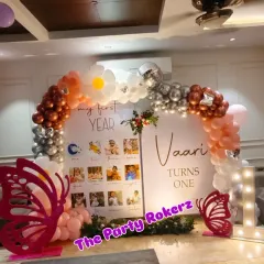 A unique take on the butterfly theme for a first birthday. This setup includes a "My First Year" photo display board, a balloon arch with daisy accents, and large pink butterfly cutouts.