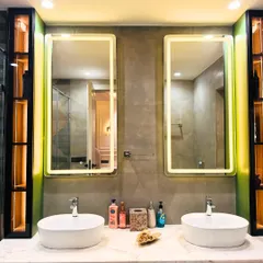 This bathroom features a double vanity with vessel sinks on a marble countertop. The backlit mirrors and integrated shelving with warm lighting add both function and a touch of spa-like luxury.