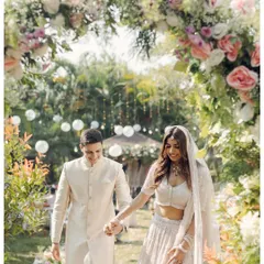 A couple walks hand-in-hand through a beautiful floral arch in their home garden. This image captures the beginning of their ceremony, a serene and personal start to their married life.