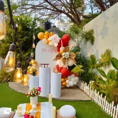A bright and cheerful anniversary or birthday setup in my garden. This design features a custom white panel with "Mr & Mrs", a vibrant red and yellow balloon arrangement, and a low picnic table for guests.