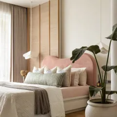 This master bedroom is a serene cocoon, anchored by a custom-designed curved headboard in a subtle peachy pink. A tactile banana fibre panel partially frames the wall, adding organic charm and texture, while bespoke pendant lights cast a delicate, intimate glow.