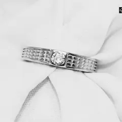 A classic men's band ring featuring a textured grid pattern and a central, bezel-set solitaire stone. This piece balances traditional design with a touch of modern detail.