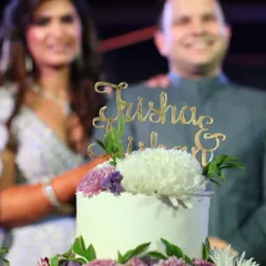 A close-up of the custom "Trisha & Nishant" cake topper on their floral wedding cake. It's these little details that make each cake unique.