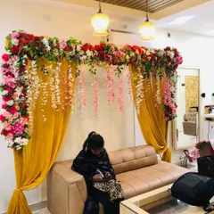 An elegant backdrop created inside a home for a small function. This setup features yellow curtains draped with a thick garland of artificial flowers, perfect for photos.