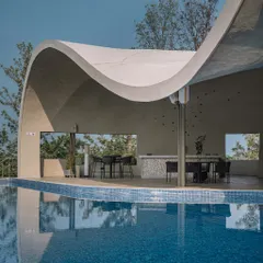 The structure of the Aqua Pool & Spa provides a covered poolside lounge and bar area, with large openings that frame the surrounding trees and hills.