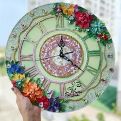 This 14-inch wall clock features a soft pistachio green base, providing a gentle backdrop for the vibrant, multi-colored sculpted flowers. The elegant black hands offer a beautiful contrast, making it easy to read the time.