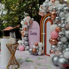 An angled view of the "Saara" naming ceremony decor. The organic balloon garland elegantly frames the custom-printed backdrop and the modern rainbow arch accent.