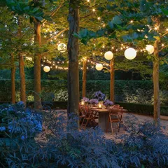 An enchanting evening dining setup beneath a canopy of trees. We installed string lights and hanging globe lights to create a warm and intimate atmosphere, perfect for alfresco dinners and entertaining.