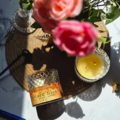 An artistic shot of the 'Nature Kiss' candle, capturing the sunlight and fresh flowers to evoke the fragrance's natural essence.