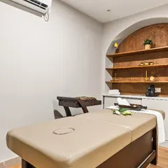 Every treatment room is a private retreat. Here, a comfortable massage bed is set against a feature wall with built-in shelving, allowing for a display of therapeutic oils and decor that enhances the holistic wellness experience.