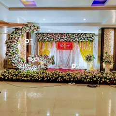 This naming ceremony stage features a crescent moon floral arrangement, adding a unique and modern touch to the traditional setup. The wide view shows the complete stage with floral pillars and backdrop.