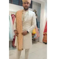 This groom is wearing a stylish ivory sherwani with subtle gold patterns. The look is completed with a peach-colored stole and a matching pagri.