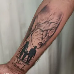 This forearm tattoo beautifully merges multiple symbols of a father's love. It combines a silhouette of his family, his son's name and birthdate, and the image of a father's hand holding his child's.