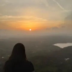 Another beautiful shot of a trekker watching the sunrise at Uttari Betta, with a lake visible in the distance.