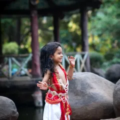 A candid, joyful photo of a boy in a Krishna costume, dancing and playing by the rocks in a park.