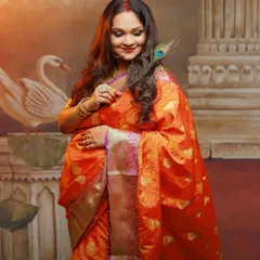 A graceful solo portrait of a mother-to-be in a vibrant orange Banarasi saree. The peacock feather adds a touch of tradition and symbolism to this elegant studio shot.
