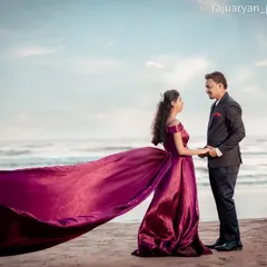 This wide shot showcases the dramatic beauty of a beach pre-wedding shoot. The bride's flowing purple gown catches the wind, creating a sense of movement and grandeur against the vast ocean.