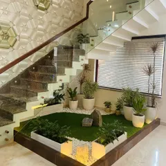 I believe every part of a home has design potential, including the space under a staircase. Here, I transformed an unused area into a tranquil indoor courtyard. This feature brings a natural element indoors with artificial turf, river stones, and potted plants, all highlighted by integrated floor lighting to create a beautiful focal point.