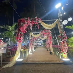 A beautiful floral entrance for an evening wedding. The combination of pink and red flowers, draped fabric, and warm fairy lights creates a romantic and inviting pathway for guests.