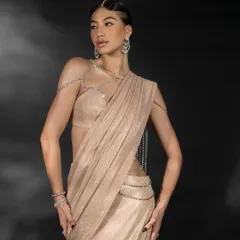 A shot from the 'Gleam Collection' featuring a shimmering beige saree. The lighting is designed to catch the metallic texture of the fabric and the sparkle of the body jewelry.