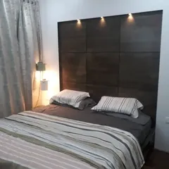 Our expertise in custom woodwork is highlighted in this elegant bedroom headboard. We crafted this dark wood paneled feature wall with integrated spotlights, creating a sophisticated focal point that provides perfect lighting for evening reading and adds a layer of architectural depth to the room.