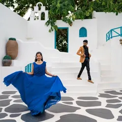 A playful and dynamic shot in a Santorini-themed location. The bride twirls her blue dress while her partner walks down the steps, creating a lively and joyful scene.