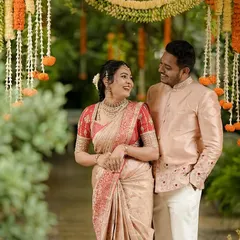 A happy couple enjoying a quiet moment during their celebration. Her beige and red silk saree is perfectly matched with his embroidered peach bandhgala jacket, showcasing our expertise in creating coordinated couple's attire.
