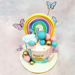 An angled view of the gender reveal cake, highlighting the vibrant rainbow topper and delicate butterfly details.