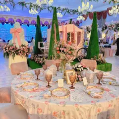 A wide view of our fairytale theme, where every element contributes to the story. The round table with floral linens and blush-toned seating is perfectly positioned to offer guests a view of the central carriage installation and oversized cake sculpture.
